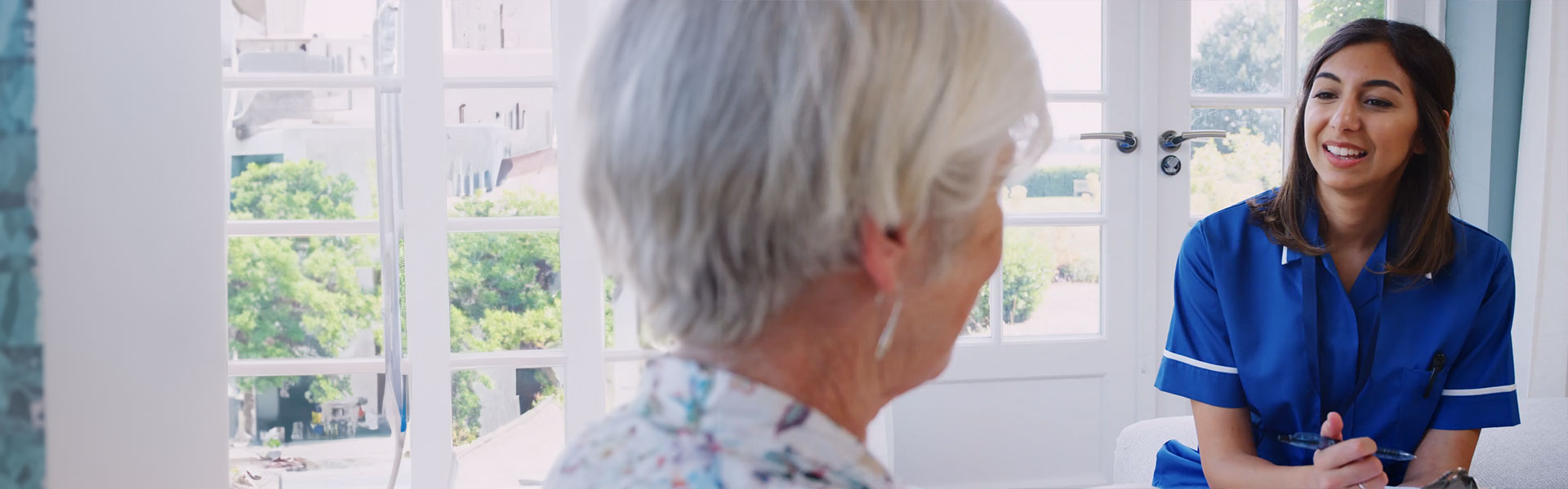 Senior woman talking to young care nurse on home visit