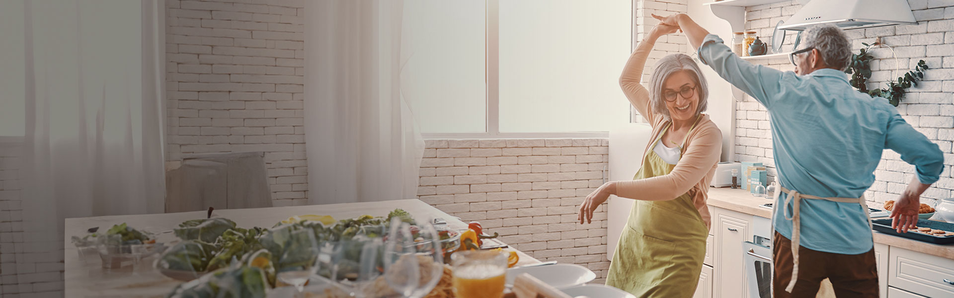 Nest Pension Services banner - Beautiful playful senior couple in aprons dancing and smiling while preparing healthy dinner at home