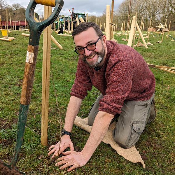 NHS SBS colleague plants a tree during a volunteering activity.