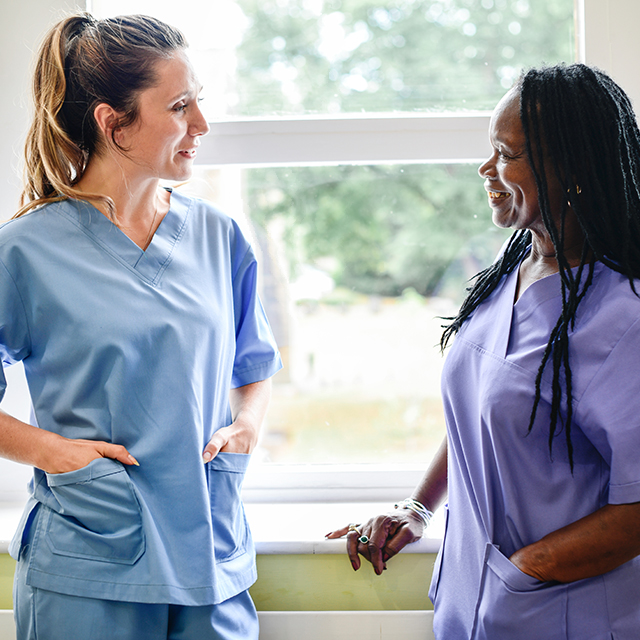 Weekly Payroll services for the NHS. Two nurses talking by a window in a hospital